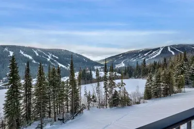 a snowy field with trees and mountains in the background at Powder Heights #18 townhouse in Sun Peaks