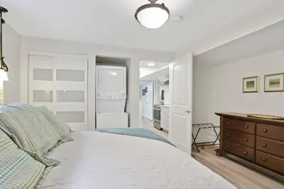 a white bedroom with a bed and a kitchen at Uncork and Unwind in West Kelowna