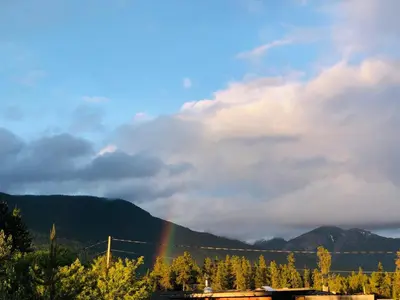 a rainbow in the sky with trees and mountains at Right Choice Home Valemount in Valemount