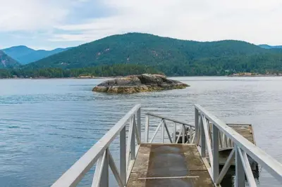 a dock on a lake with a rock in the water at Exclusive Private Island - Pacific Ocean Paradise in Madeira Park