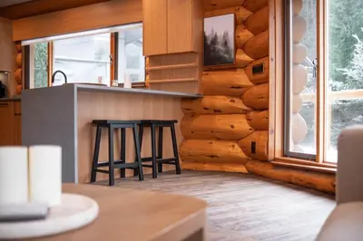 a kitchen with a counter and stools in front of a log wall at Snowridge Chalet by Outpost Whistler in Whistler