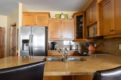 a kitchen with wooden cabinets and a stainless steel refrigerator at The Aspens 5 w/ Hot Tub in Big White