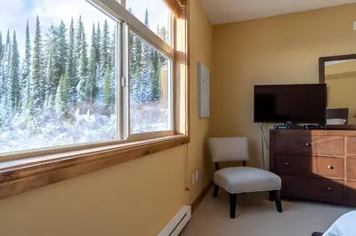 a bedroom with a window and a dresser and a television at The Aspens 5 w/ Hot Tub in Big White