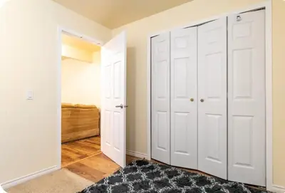 a bedroom with white closet doors and a rug at Basement Room in Calgary