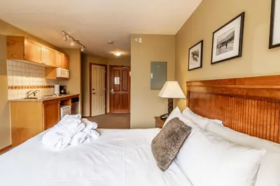 a bedroom with a white bed and a kitchen at Cascade by Elevate Vacations in Whistler