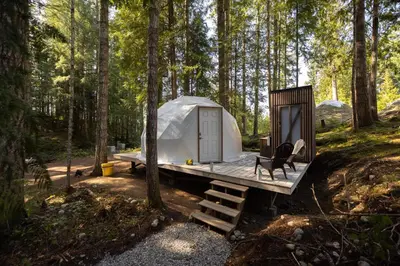 a tent in the woods with a bench and a chair at Stay Wilder Sunshine Coast in Sechelt