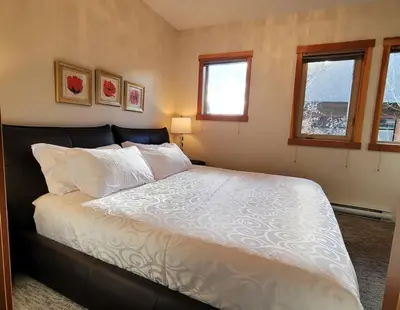a bedroom with a bed with white sheets and two windows at Mountain Escape sleeps 10 Guests in this 3BD 2BT Top Floor Condo with Mountain View in Canmore