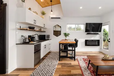 a kitchen with white cabinets and a wooden table at Coastal Creative Garden Studio in Colwood