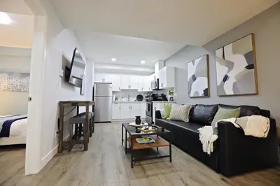a living room with a black couch and a kitchen at Queen Suite 20 Min from YEG Airport with Disney in Edmonton