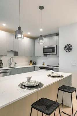 a kitchen with white cabinets and a counter with two stools at Revelstoke Alpine Retreat - RARE One-Bedroom Condo in Revelstoke