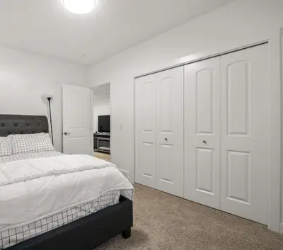 a bedroom with white walls and a bed with white cabinets at Angie’s place in Calgary