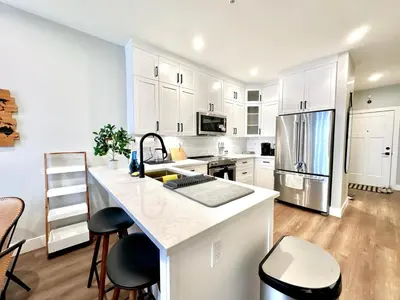 a kitchen with white cabinets and a kitchen island with stools at Dreamy Panoramic Lakeview 1 Bedroom plus Den in Harrison Hot Springs
