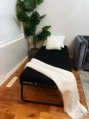 a black ottoman sitting on a floor with a plant at La Maison in Vancouver