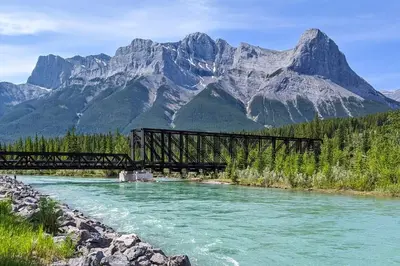 a bridge over a river with mountains in the background at The Mountain Loft in Canmore