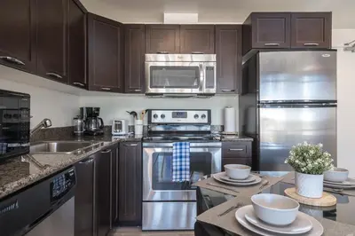 a kitchen with stainless steel appliances and wooden cabinets at UC Stampede Condo by Train, Hospital, free UG parking & Gym, AC, full kitchen in Calgary