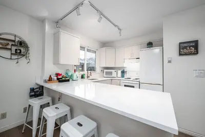 a white kitchen with white appliances and stools at Luxurious Retreat/Hot Tub/Mountain View/4 Beds in Canmore