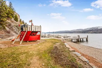 a red boat on the shore of a body of water at Beautiful Cabin Right next to Lake Okanagan #5 in West Kelowna