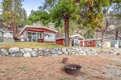 a red house with a stone wall in front of a yard at The Perfect Getaway Cabin in the Okanagan #6 in West Kelowna
