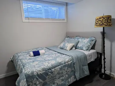 a bedroom with a bed with blue sheets and a window at The Fruitful Vineyard- A Beautiful 2 Bed Suite in Calgary