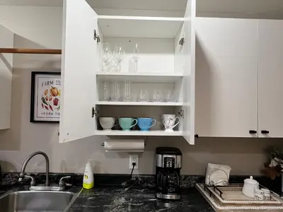 a kitchen counter with white cabinets with cups and dishes at Yellow Door Suite in Campbell River