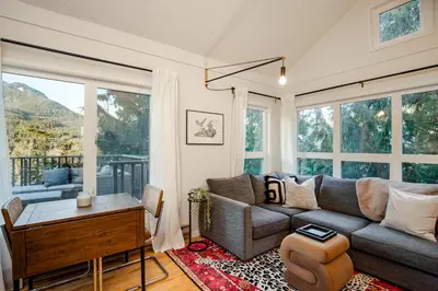 a living room with a couch and a table and windows at 1BR plus Loft in Gondola Village, Creekside, Amazing Patio with Views, Near Gondola, Free Parking in Whistler