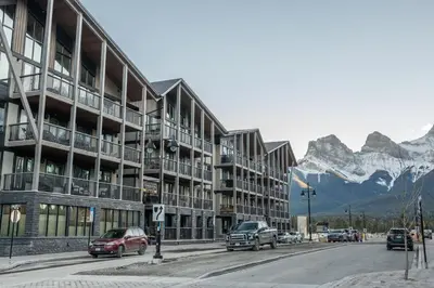 a street with cars parked in front of a building with mountains at Timberstone Condo by Canadian Rockies Vacation Rentals in Canmore