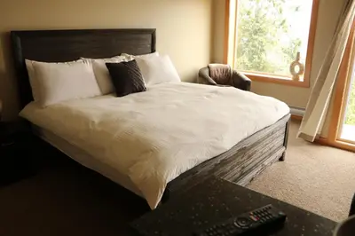 a bed with white sheets and pillows next to a window at Moon Water Lodge in Malahat