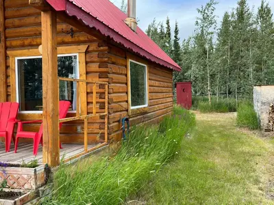 a log cabin with red chairs on a deck at Dry Log Cabin with Mountain Views in Upper Laberge