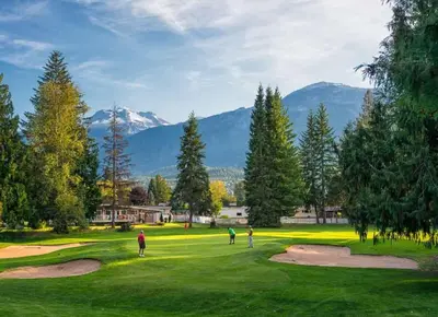 people playing golf on a golf course with mountains in the background at Tucker's Place in Revelstoke