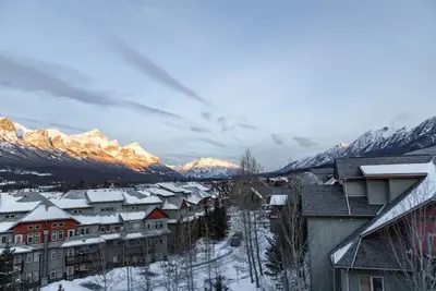 a town with snow covered buildings and mountains at Magnificent Mountain Penthouse - Hot Tub & Pool managed by Little Sister Getaways in Canmore