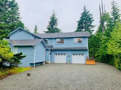 a blue house with a dog standing in front of it at Blue Cedar Suite in Tofino