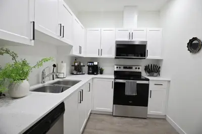 a white kitchen with a sink and a stove at Elegant Escape with King Bed, Long Stays, WEM, Disney in Edmonton