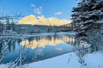 a bridge over a river with snow covered mountains at #202 Cozy Mountain View 2 bedrooms in DT in Canmore