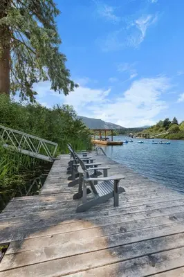 a row of benches sitting on a wooden dock next to the water at Riverside by Cowichan Lake Cottages in Lake Cowichan
