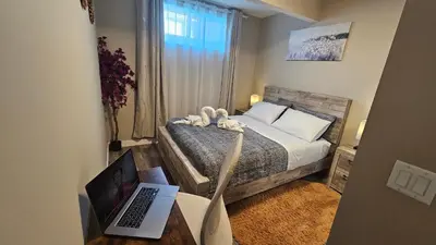 a small bedroom with a bed and a laptop on a desk at Luxury Basement Suite with 2 Bedrooms, 2 Queen Beds, Free Wi-Fi, and Free Parking in Calgary