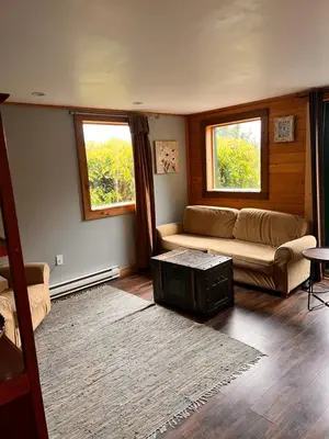 a living room with a couch and a table and two windows at Bear Cove Cottages in Port Hardy