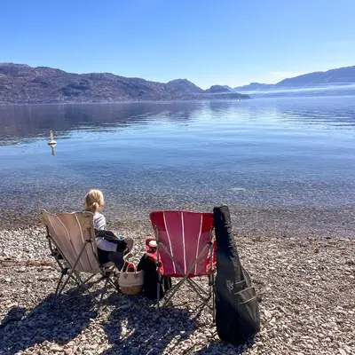 a child sitting in a chair on a beach at Kelowfornia Lakeview Retreat in Kelowna