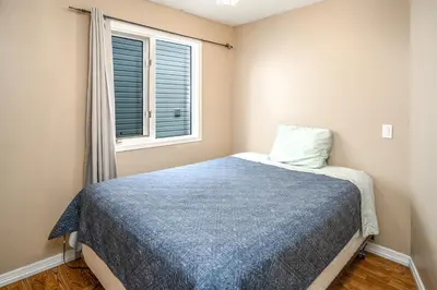 a bedroom with a bed with a blue blanket and a window at Airport 4BR2BA Mainfloor Suite 1min walk to bus stop in Calgary