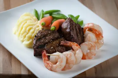 a plate of food with steak and shrimp and vegetables at Hotel Clique Calgary Airport in Calgary