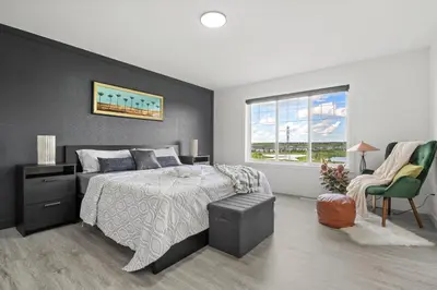 a bedroom with a bed and a chair and a window at LUXURY LAKEVIEW HOME - 2500sqft of private space with 5 Beds, 4 Bath, 2 Living Rooms, Kitchen, AC, Jacuzzi, 10 Guests Max, Basement Not Included, 18-min to Airport, 20-min to Downtown, 80-min to Banff in Calgary