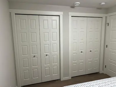 two white closet doors in a room with a bed at The Haven - cozy 1 bedroom suite in Seton SE Calgary in Calgary