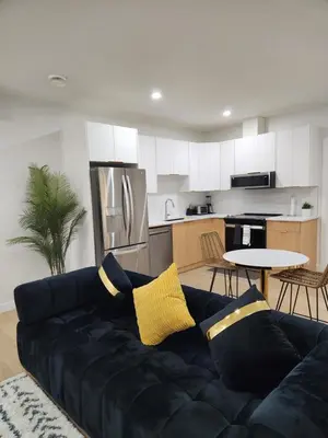 a living room with a black couch and a kitchen at Brand New Deluxe 2 Bedroom Suite with AC & Den in Calgary