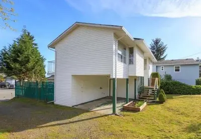 a white house with a garage in a yard at Entire home minutes from 3 lakes and a river! in Nanaimo