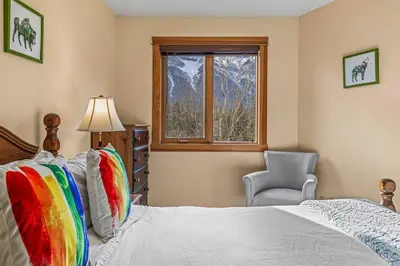 a bedroom with a bed and a chair and a window at C303 Hidden Gem with MTN andCreek View, Quiet and Private in Canmore