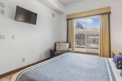 a bedroom with a bed and a chair and a window at S105 Canmore Stay- Hot tub, stream rm, gym, parking Mtn Retreat in Canmore