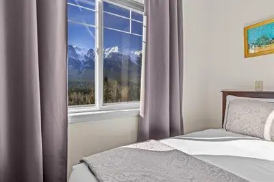 a bedroom with a window with a mountain view at B212 Hot Tub, AC x3, parking, 2 min to Banff Gate in Canmore