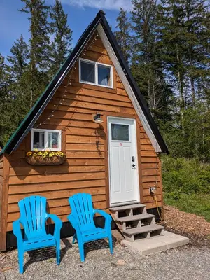 two blue chairs sitting in front of a cabin at Farmhouse cabin on 33 acre farm in Powell River
