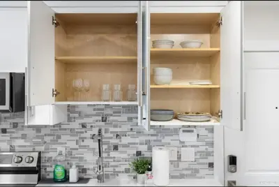 a kitchen with white cabinets and dishes on shelves at Entire new small home in Vancouver