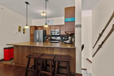 a kitchen with wooden cabinets and a counter with stools at Settler's Crossing #56 ski-in ski-out condo with private hot tub in Sun Peaks
