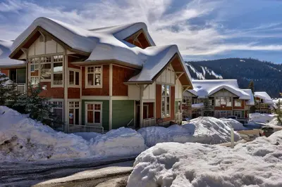 a house covered in snow with piles of snow at Settler's Crossing #56 ski-in ski-out condo with private hot tub in Sun Peaks